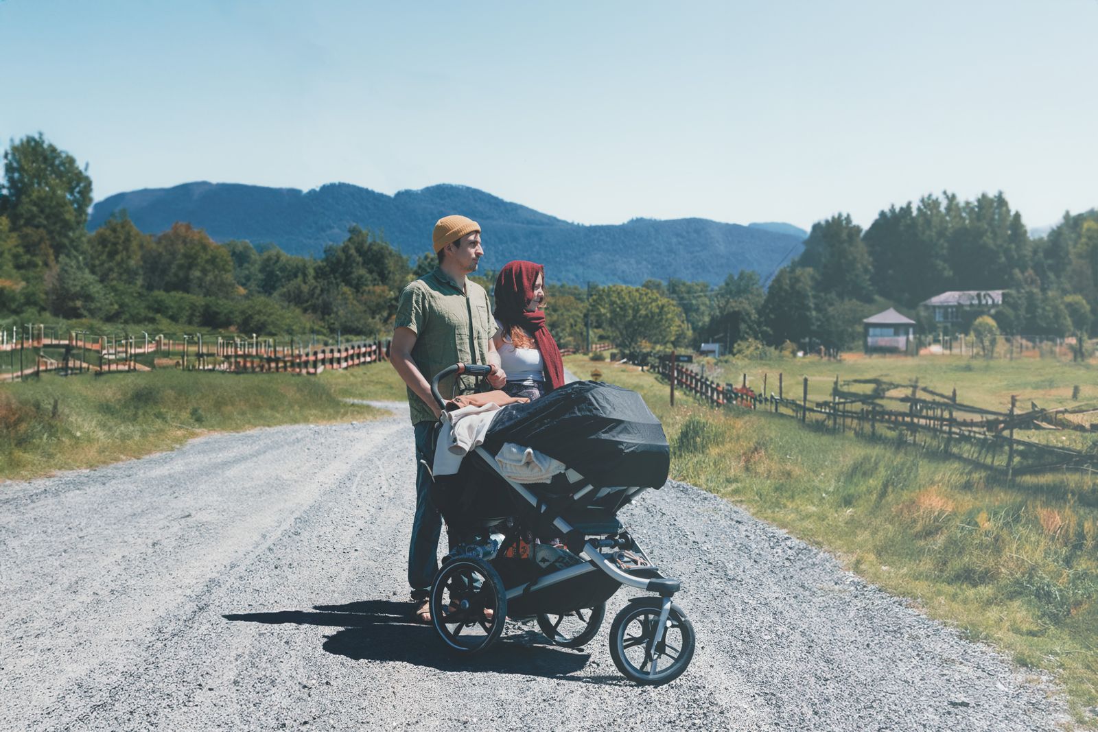 Par med joggevogn på en solfylt landevei mot fjell